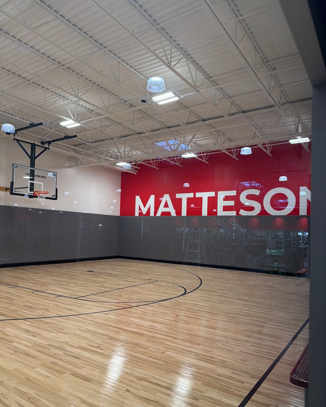 Hardwood basketball court at VASA Fitness Matteson with a red Matteson wall graphic and the ceiling structure left exposed overhead